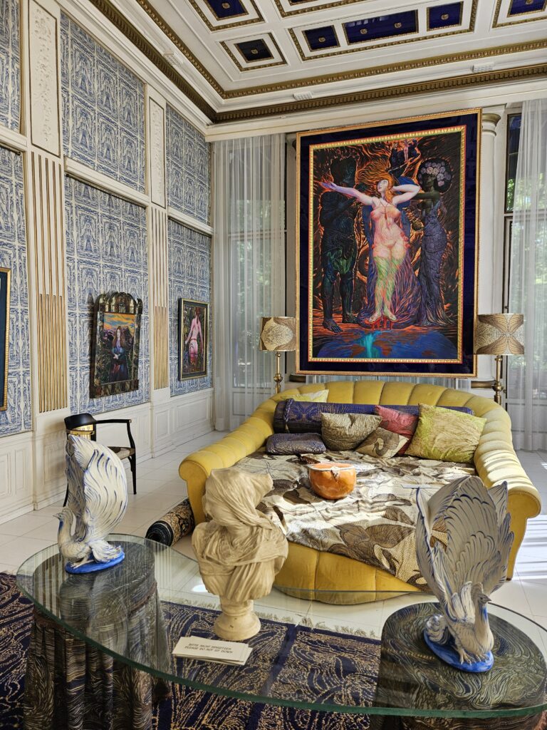 A vibrant living room inside the Otto Wagner Villa, featuring a yellow couch, modern art, intricate wall designs, and decorative sculptures, showcasing the eclectic mix of Art Nouveau and contemporary elements.