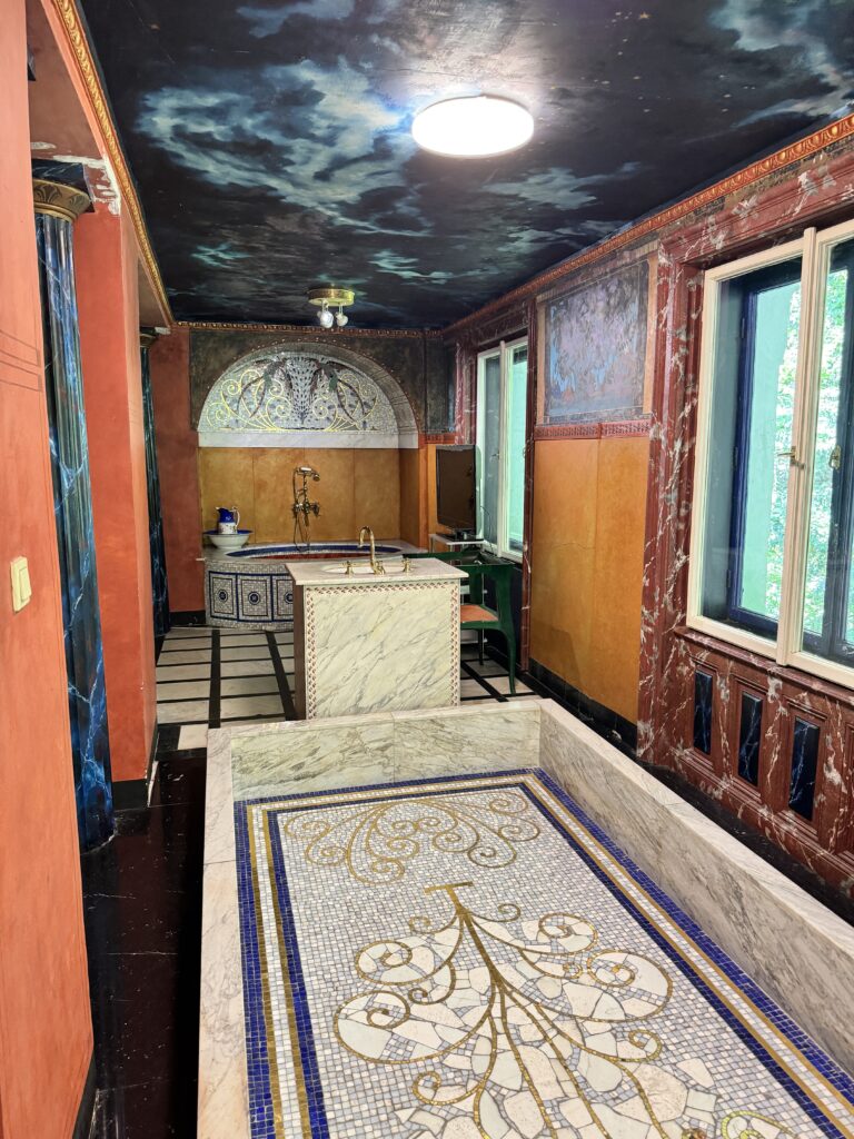 A luxurious bathroom inside the Otto Wagner Villa, featuring intricate mosaic flooring, marble surfaces, and a painted ceiling resembling a night sky, showcasing the villa's opulent Art Nouveau design.