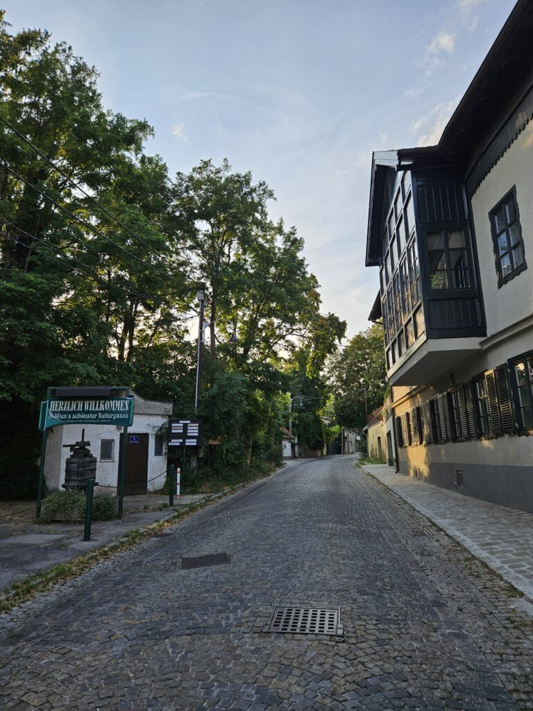 A quaint, cobblestone street in Stammersdorf, lined with trees and traditional buildings, offering a welcoming entrance to the historic wine district.