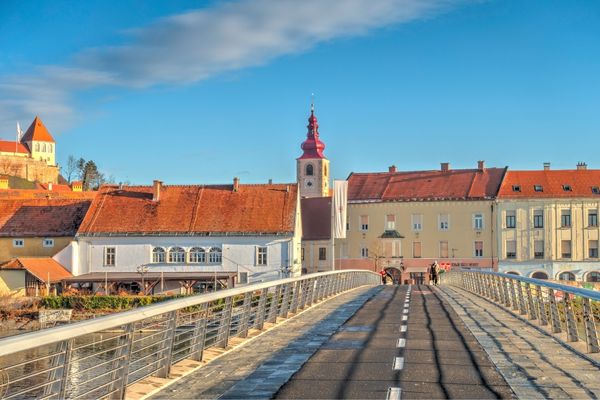 View of the footbridge leading into Ptuj’s old town, Slovenia, with the clock tower and Ptuj Castle in the background.