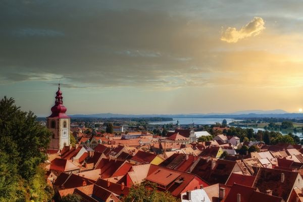 Sunset view of Ptuj, Slovenia, with red rooftops, the clock tower, and the Drava River in the background.