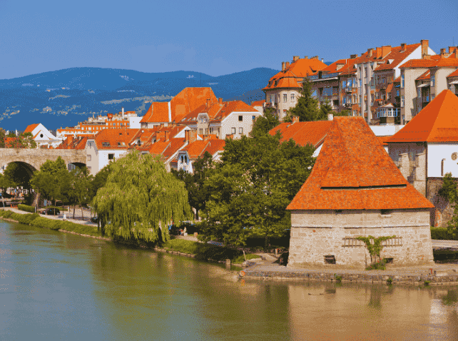 Maribor riverside with historic tower and red-roofed buildings.