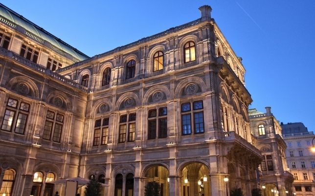Vienna State Opera building illuminated at dusk. Next to it the Best Wurst in Vienna